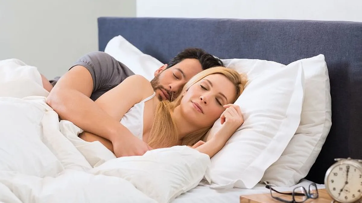 Casal na cama, com a mulher acordada olhando o despertador