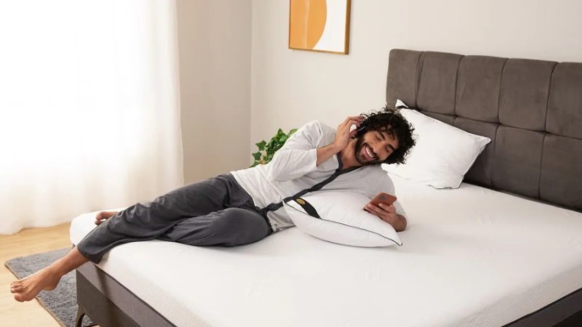 Homem cochilando de lado sobre a cama, vestido com roupa de dia